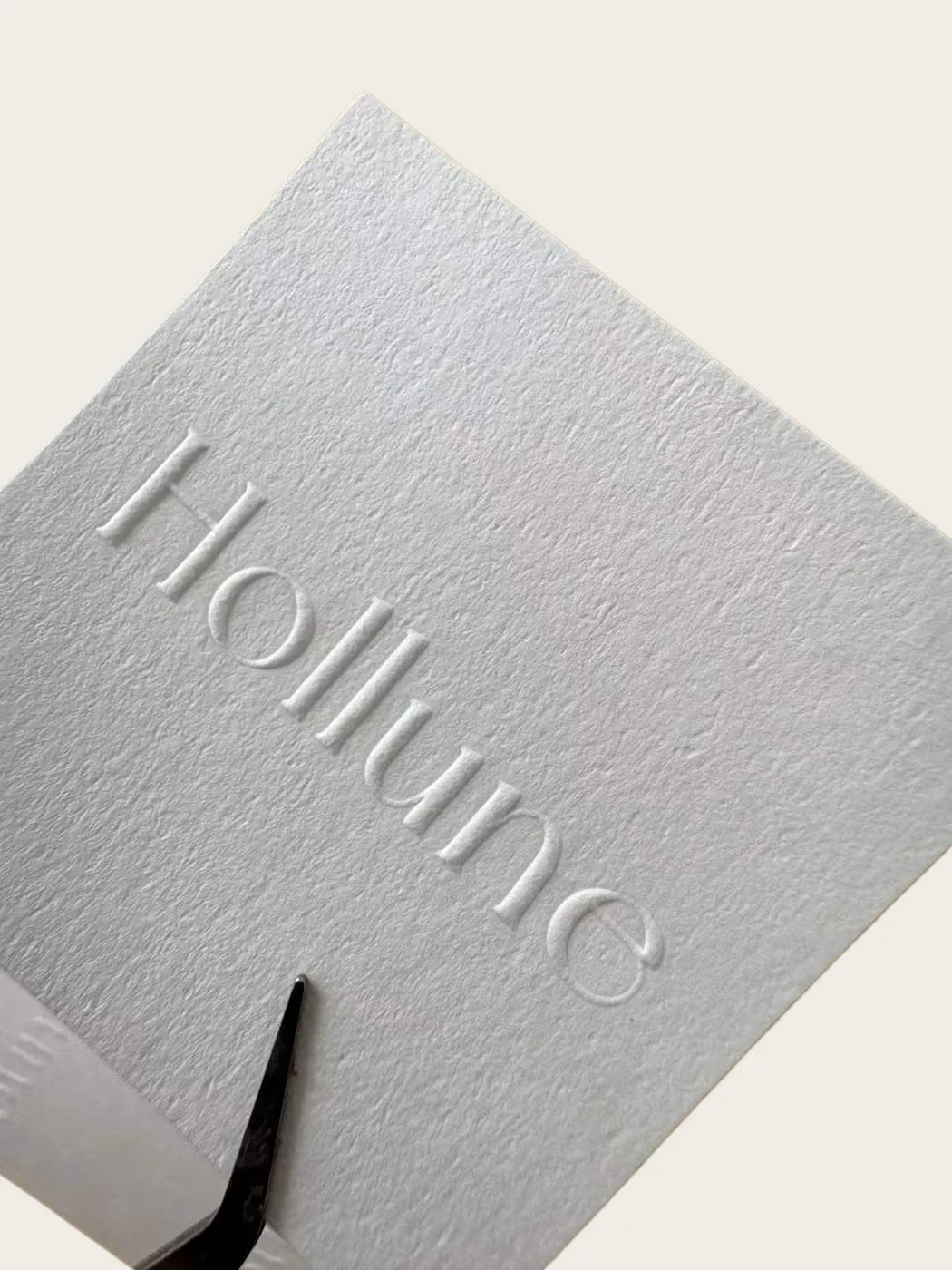 Close-up of a white textured paper label with a raised embossed wordmark.
